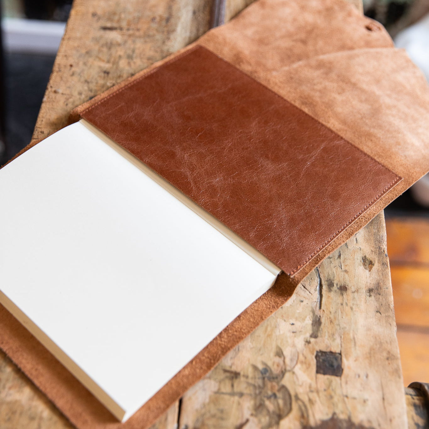 Notebook with a brown leather cover and refillable pocket on a rustic wooden surface