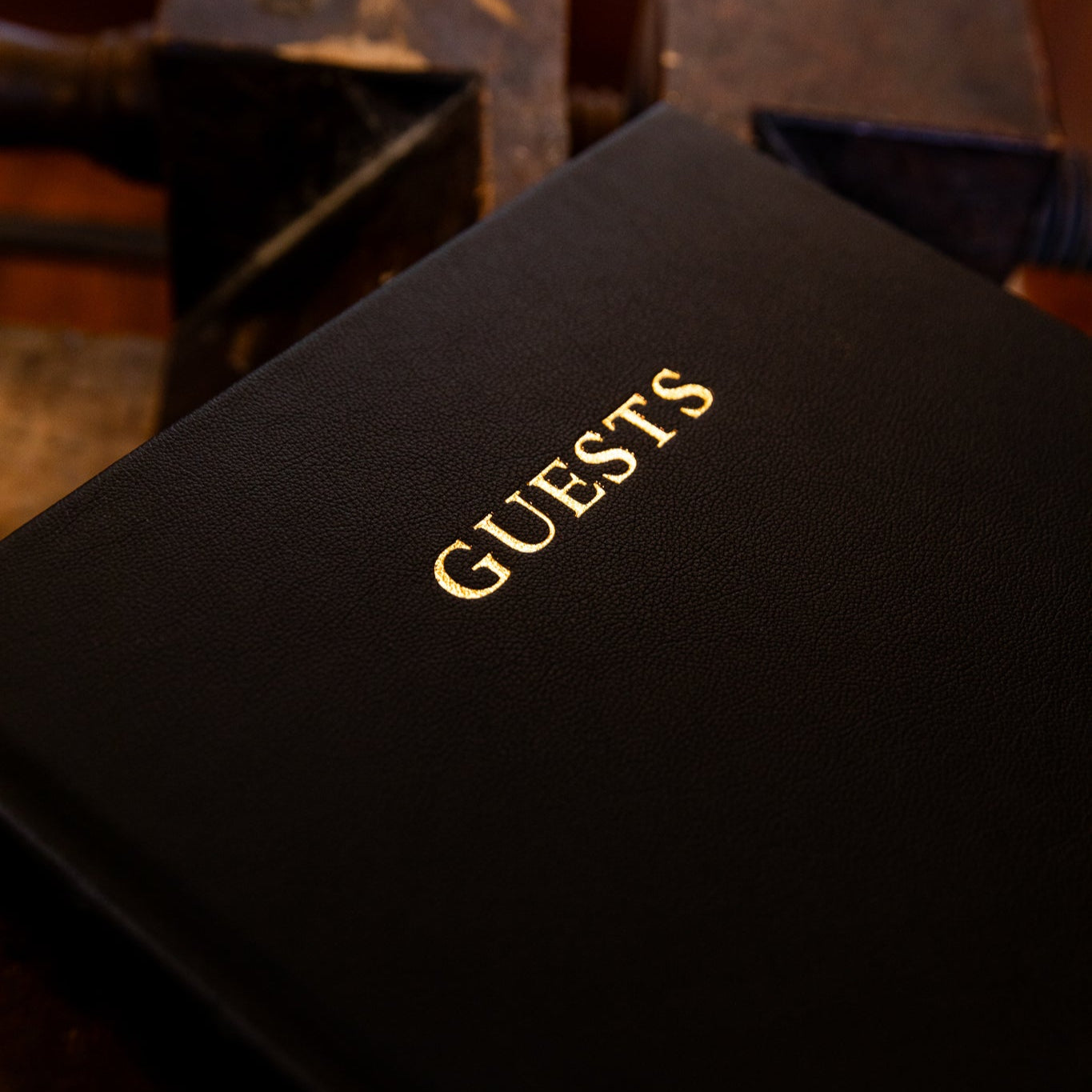 Black guest book with 'GUESTS' in gold lettering on a wooden surface.