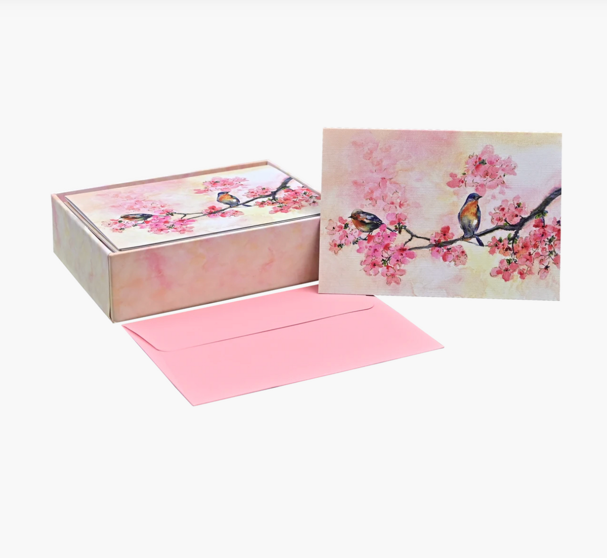 A boxed greeting card set with a pink envelope, featuring cherry blossom artwork and two small birds on the box lid and front card, photographed on a clean white background.