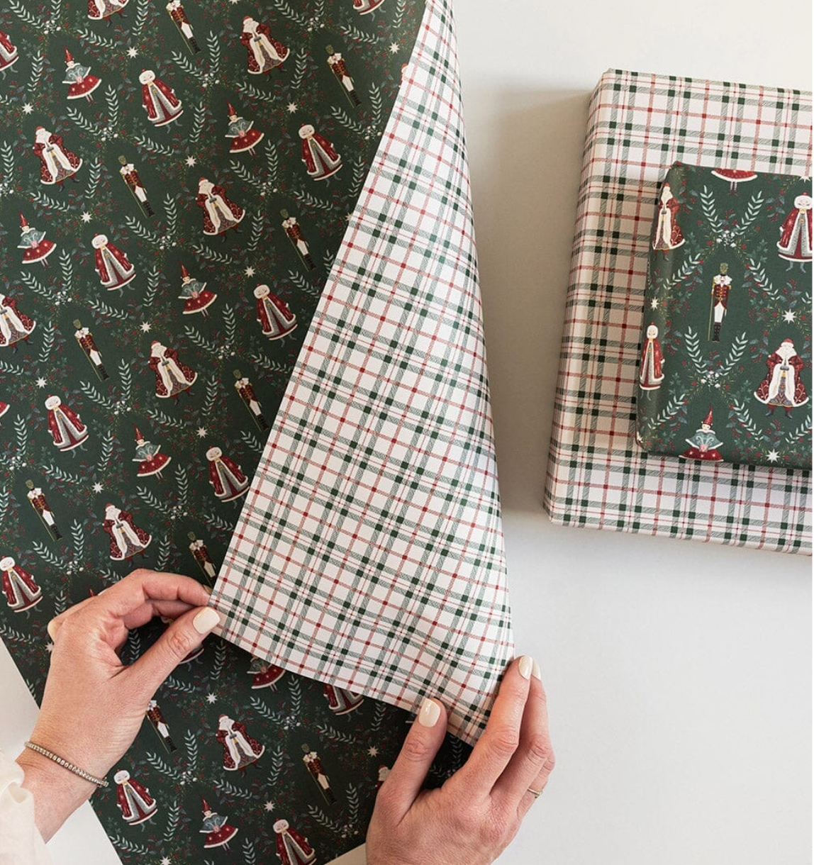 Hand holding a piece of fabric with Christmas-themed pattern next to wrapped gifts.