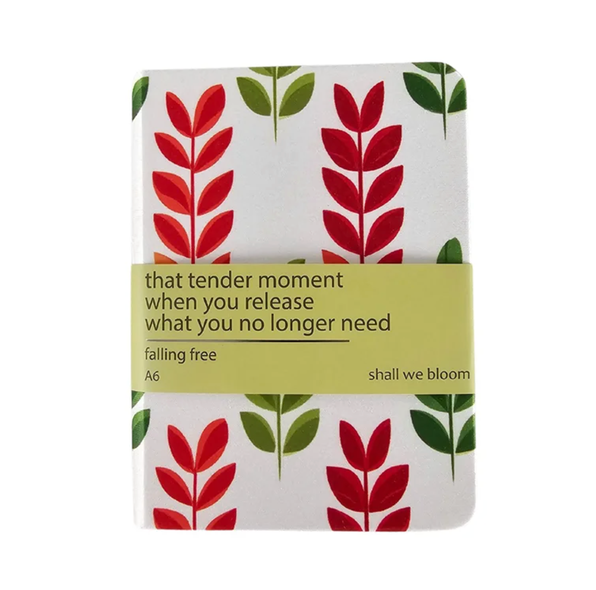 A small A6 notebook with a white cover decorated with red and green botanical leaf patterns, wrapped in a light yellow-green paper band with the text 'that tender moment when you release what you no longer need falling free shall we bloom'.