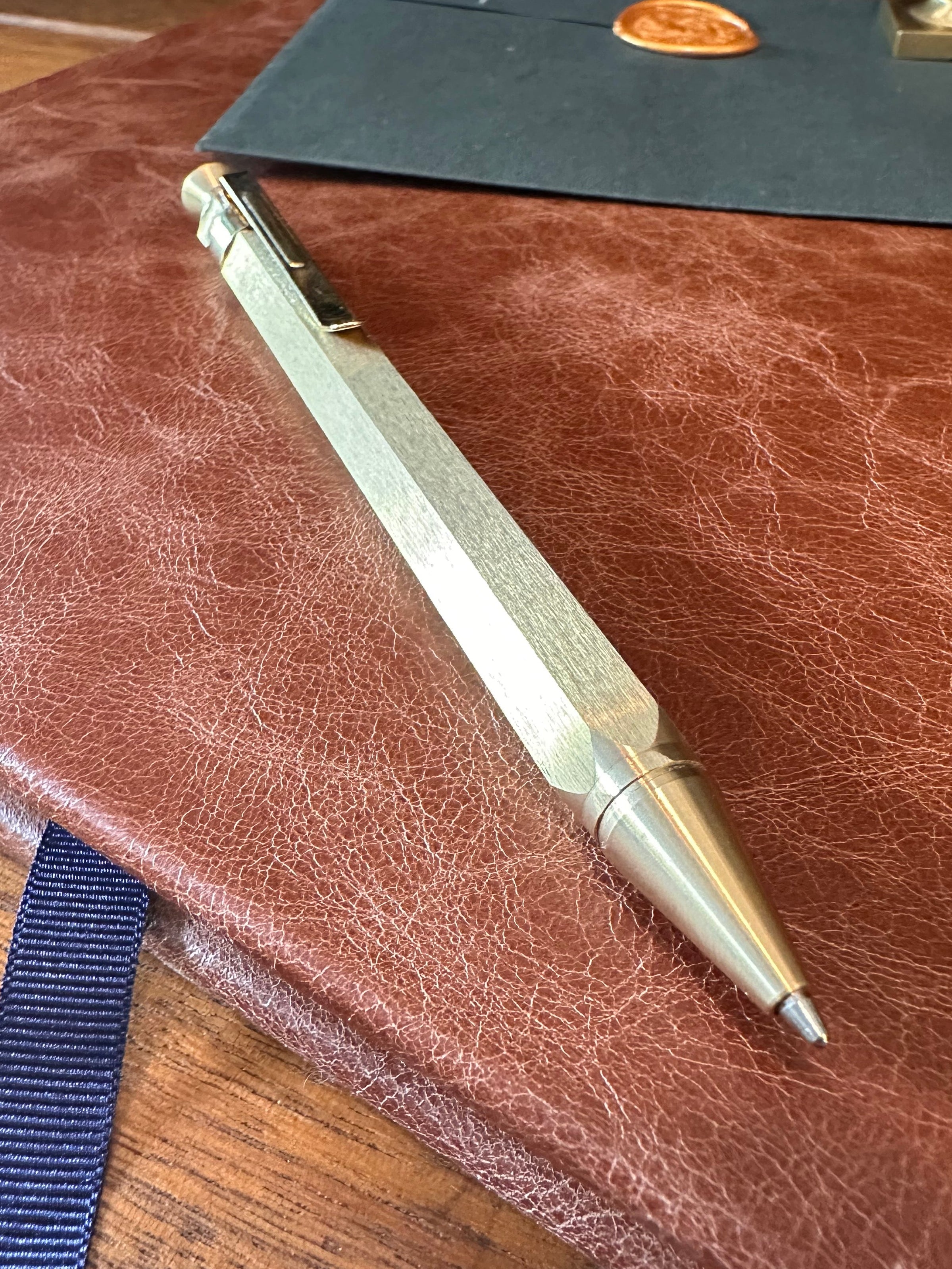 Gold pen on a brown leather surface with a wooden stand in the background