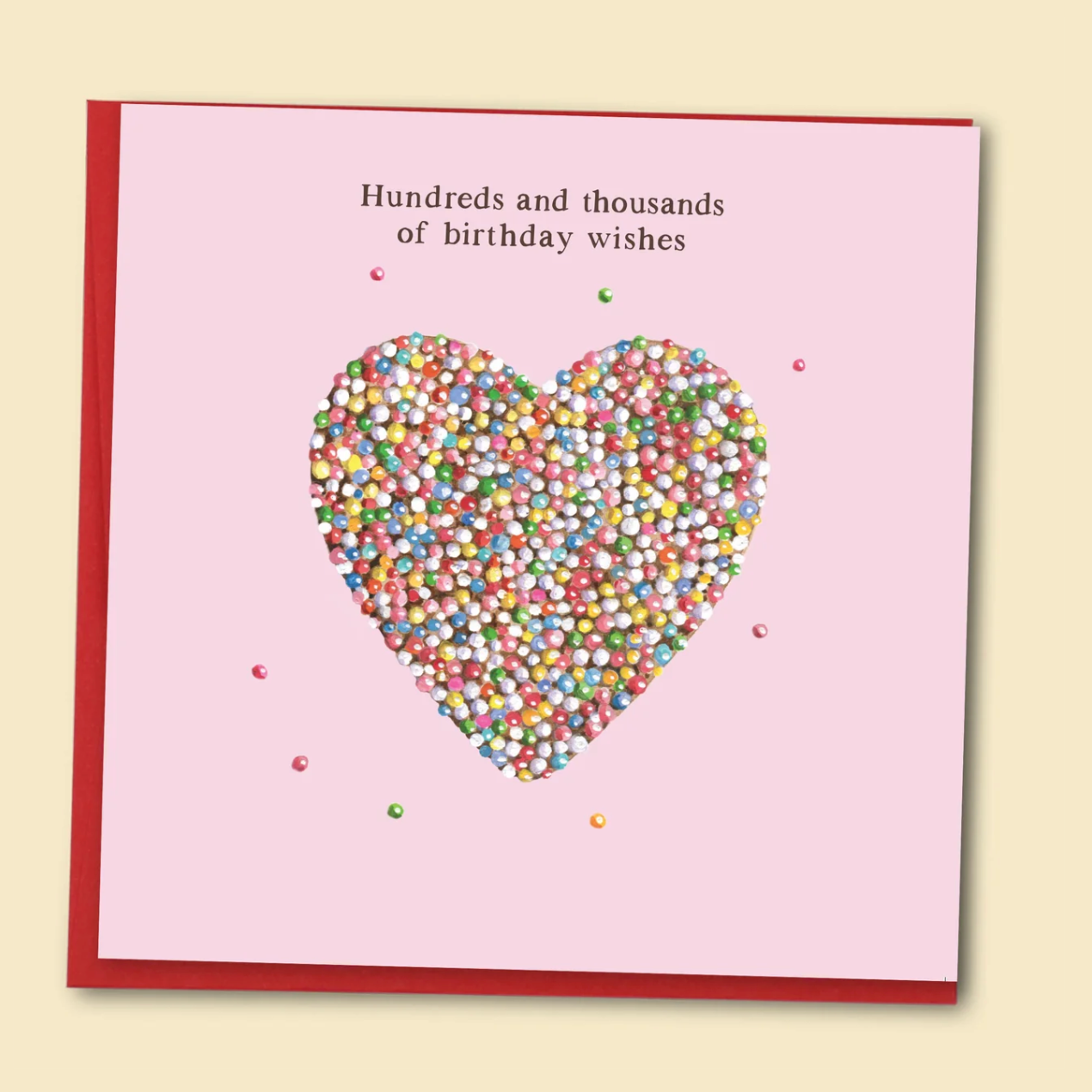 A square pink birthday card with a red border, featuring a heart-shaped confetti design in the center and the text 'Hundreds and thousands of birthday wishes' at the top, shown on a light beige background.