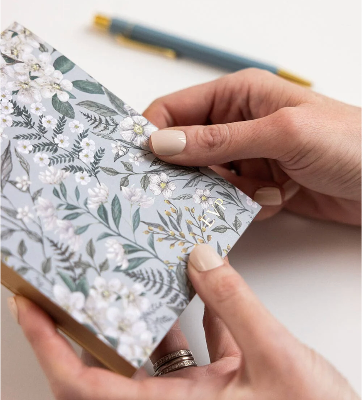 Person holding a floral notebook with a pen on a light background