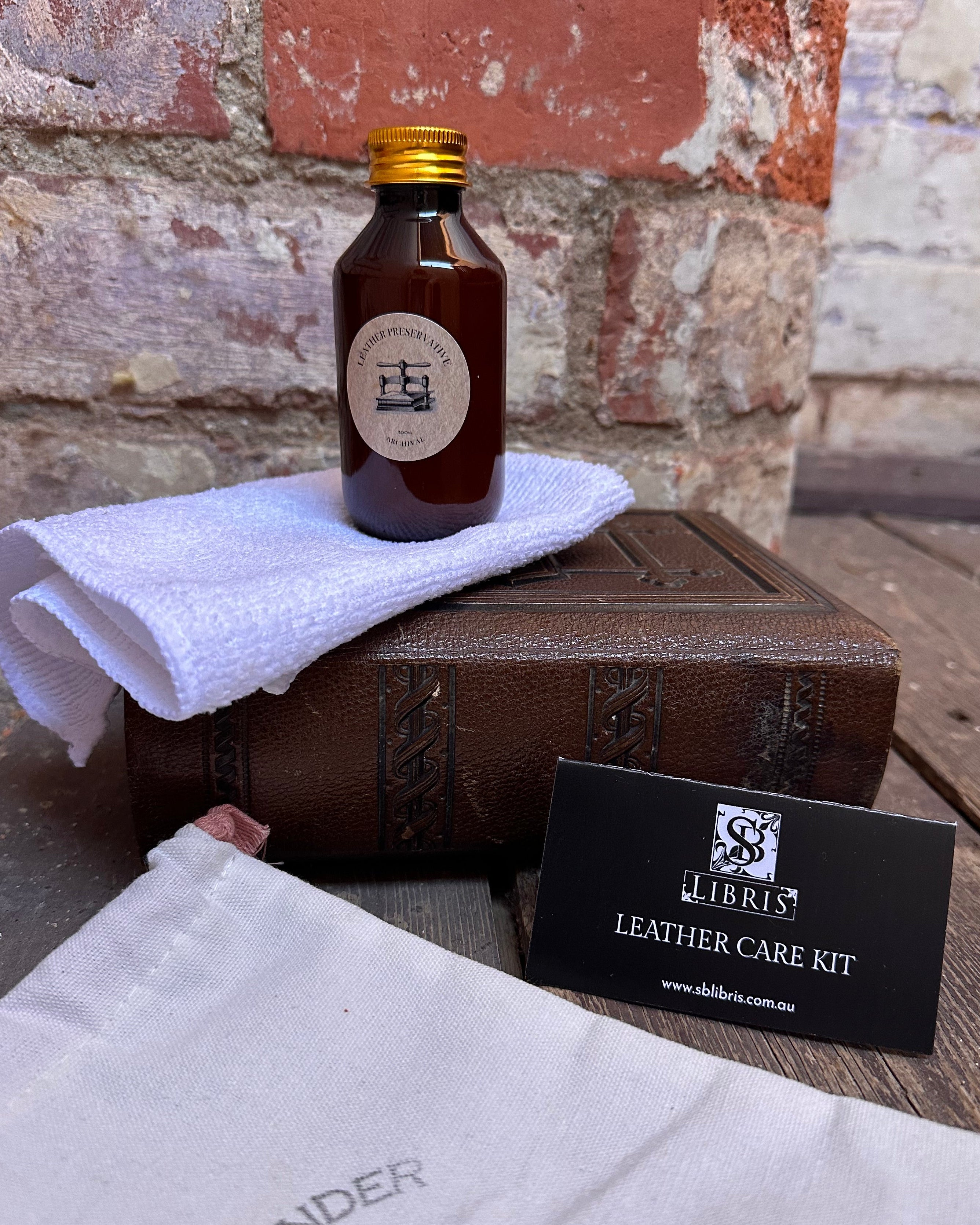 Leather care kit with bottle, towel, and box on a stone surface
