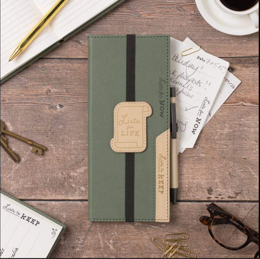 Green notebook with a decorative strap on a wooden surface with stationery items.