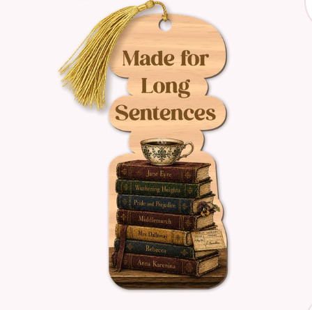 A wooden bookmark with a gold tassel, featuring the engraved text 'Made for Long Sentences' above an illustration of a stack of books and a teacup.