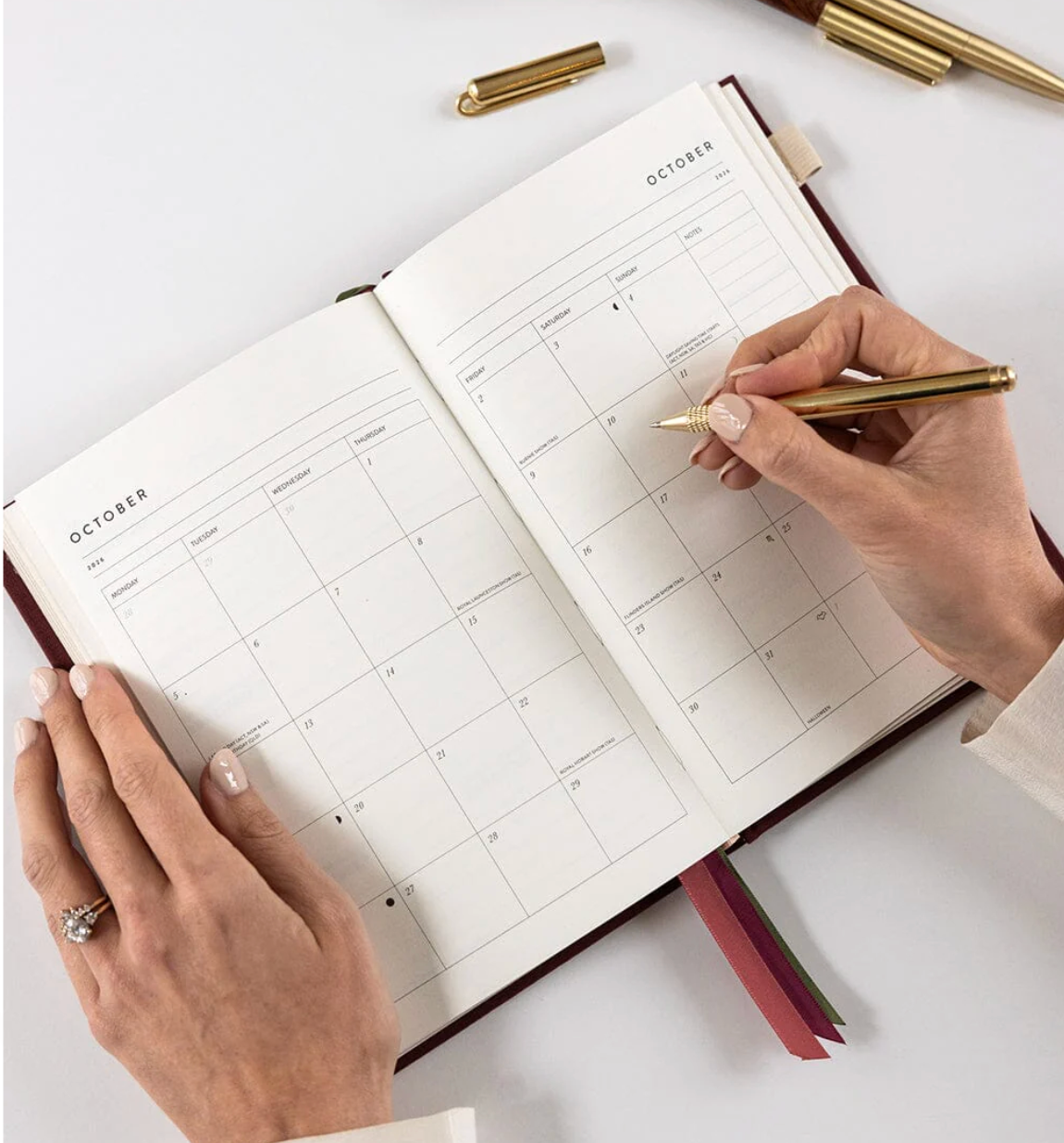 Person using a planner with a gold pen on a white surface