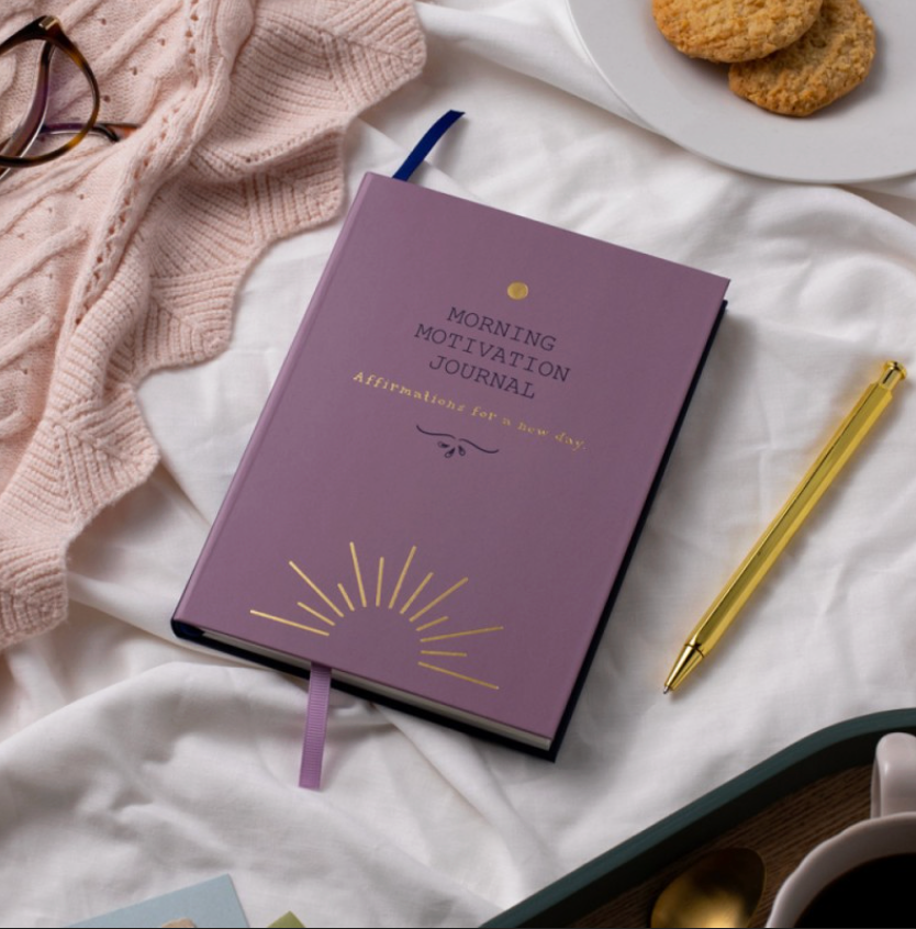Purple 'Morning Motivation Journal' on a white surface with a pen and cookies.