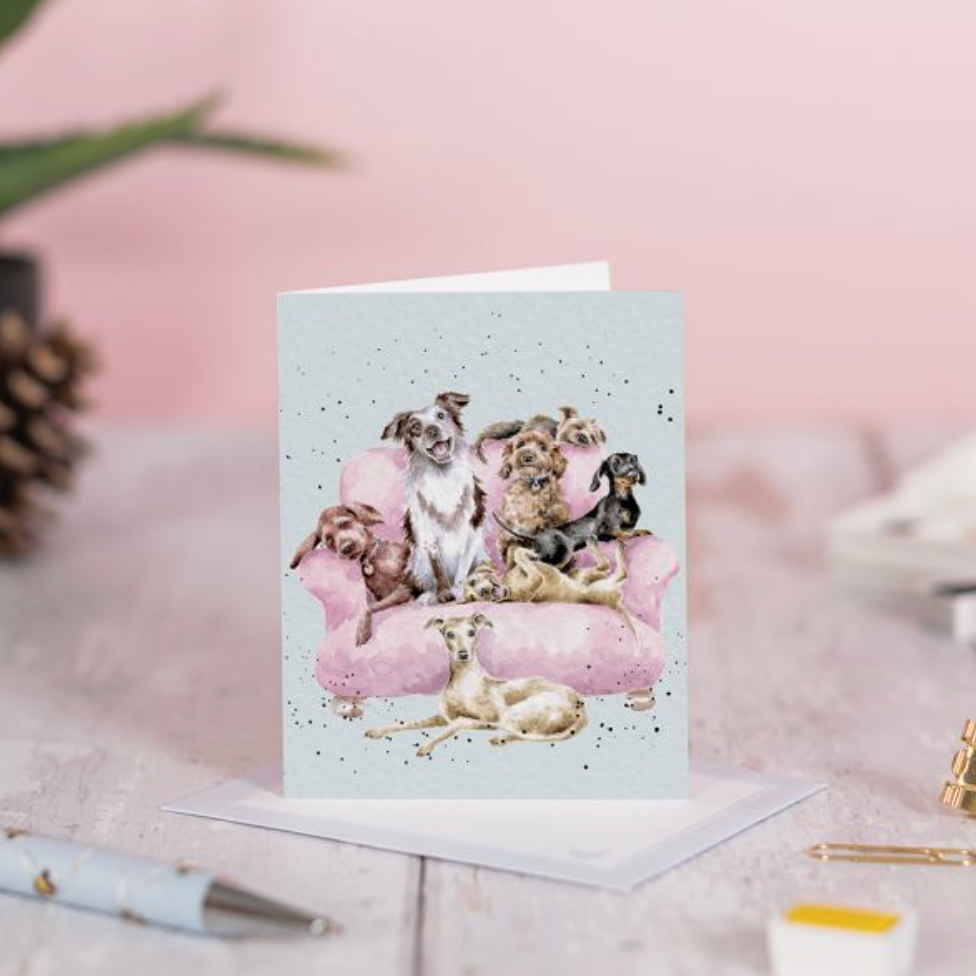 Greeting card with puppies on a pink couch on a light pink surface.