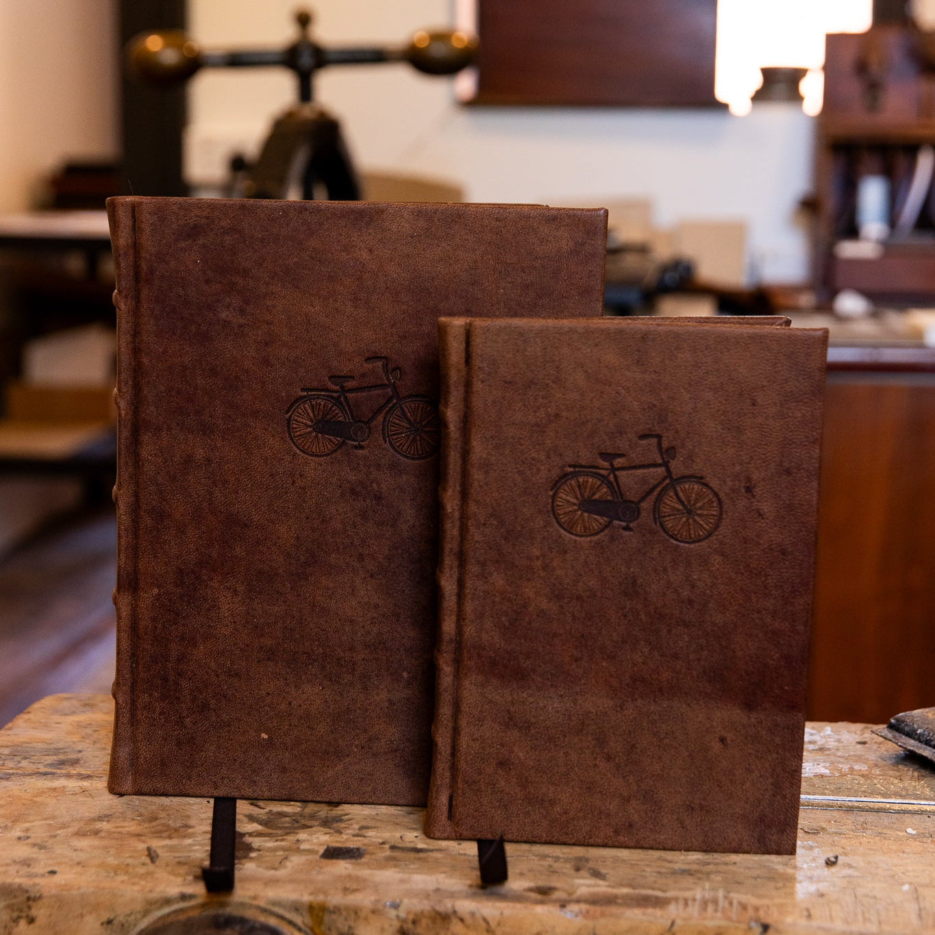 Two handcrafted leather 'On Ya Bike' journals by SB Libris, featuring vintage bicycle embossing in large and small sizes.